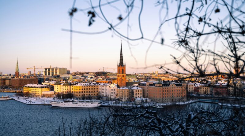 Things to do in Stockholm showing Gamla Stan old town colourful buildings reflected in the water with Stockholm City Hall tower visible in the background at sunset