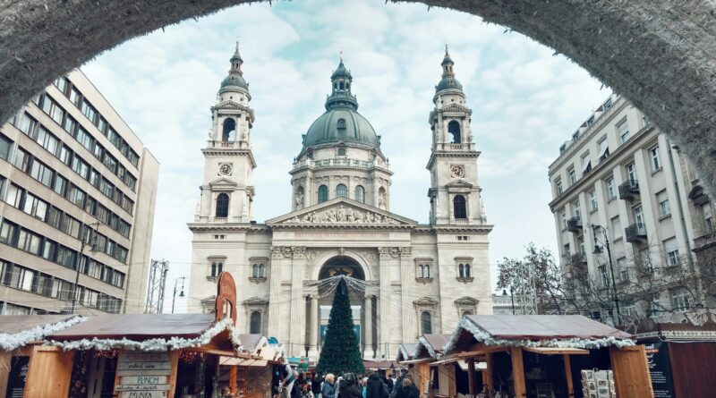 Budapest Christmas market at St Stephen's Basilica showing the illuminated Gothic facade of the basilica behind decorated market stalls with warm lights and a large Christmas tree representing the best Christmas market in Budapest