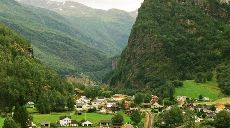 Flam Norway village nestled at the end of the Aurlandsfjord surrounded by steep mountain slopes and waterfalls with the Flamsbana railway station visible in the foreground